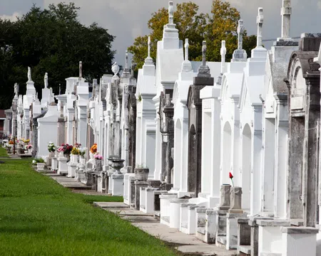 Row of white and gray above-ground tombs with flowers in a cemetery on a sunny day.