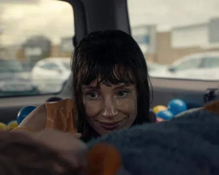 Woman with wet hair smiling inside a car filled with colorful plastic balls, looking at someone out of focus.