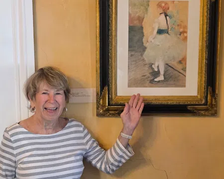 Smiling elderly woman pointing at framed impressionist painting of ballerina in museum setting