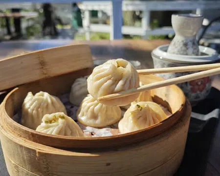 Chopsticks picking up a steamed dumpling from a bamboo basket on a wooden table outdoors