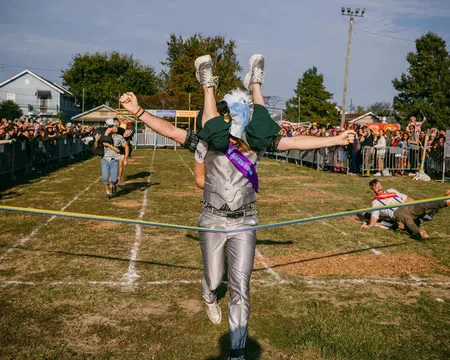 Person in eagle costume winning a race while carrying another runner across the finish line at outdoor event.