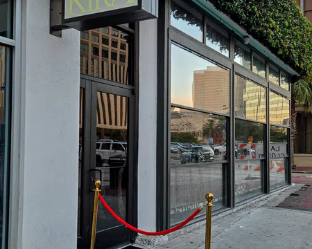 Entrance to KIRA with black door, red velvet rope, gold stanchions, and green ivy on urban building facade.