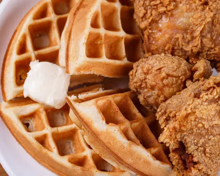 Crispy fried chicken pieces served with golden waffles and a dollop of melting butter on a white plate.