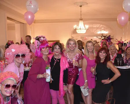 Group of women dressed in pink and black at an indoor party with balloons and drinks celebrating together.