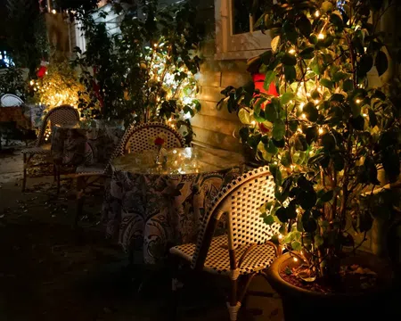 Cozy outdoor cafe seating with patterned chairs and tables lit by warm string lights at night.
