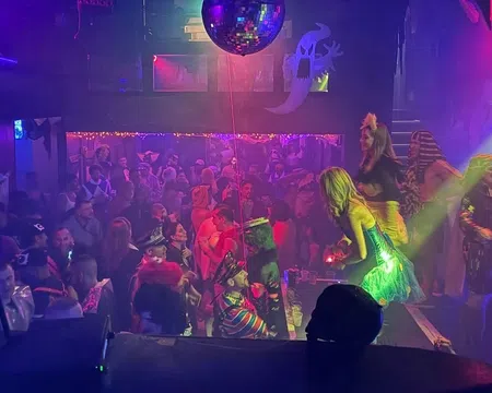 Crowded nightclub with people dancing and colorful lights under a large disco ball during a party