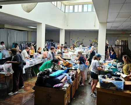 Volunteers sorting and organizing clothing donations in a large, well-lit community center with boxes and racks of clothes.