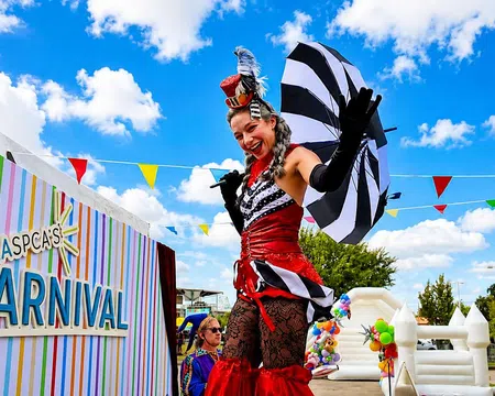 Performers in colorful carnival costumes entertain at LASPCA's outdoor community carnival event under a bright blue sky.
