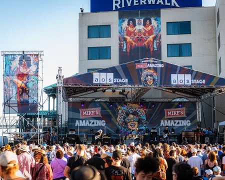 Outdoor music festival on Mike's Amazing stage at Riverwalk with large crowd enjoying live band performance.