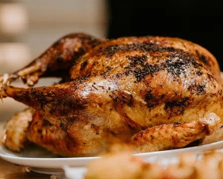 Golden-brown roasted whole chicken with herbs on a white plate ready to serve.