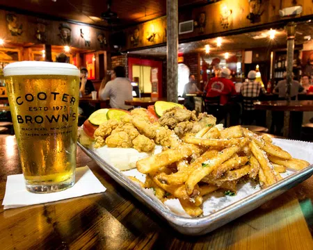 Fried seafood platter with fries and a cold beer glass on a wooden table in a cozy bar setting.