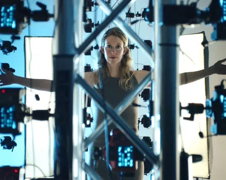 Woman standing inside a 3D scanning rig with arms outstretched surrounded by cameras and lighting panels.