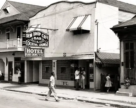 Black and white street scene with Dew Drop Cafe bar, cocktail lounge, hotel, and people walking and standing outside.