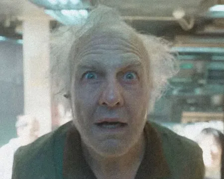 Older man with wild white hair and surprised expression looking directly at the camera indoors.