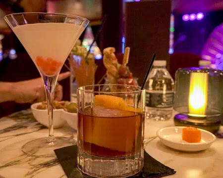 Cocktails served on a marble table with dim lighting and a water bottle in a cozy bar setting.