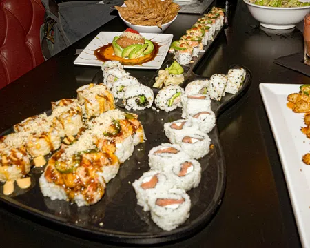 Assorted sushi rolls with sauces and garnishes served on a black platter and white plates on a dark table.