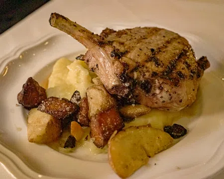 Grilled pork chop served with mashed potatoes and roasted vegetables on a white plate