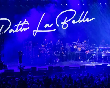 Patti LaBelle performing live on stage with band and blue lighting, audience visible in front of the stage