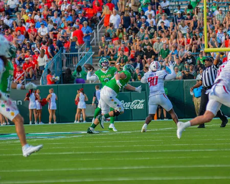 Tulane quarterback prepares to throw under pressure from defenders with crowd and cheerleaders in background