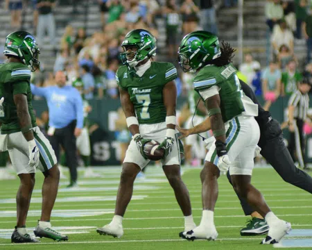 Tulane football players in green uniforms huddle on field during game with crowd in background