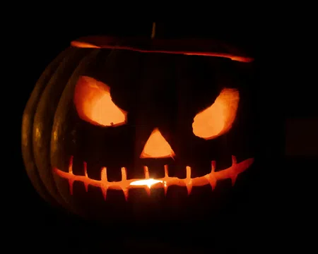 Glowing Halloween jack-o'-lantern with menacing eyes and stitched mouth carved in pumpkin in darkness