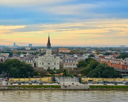 Stunning view of St. Louis Cathedral and Jackson Square with the Mississippi River in the foreground at sunset.