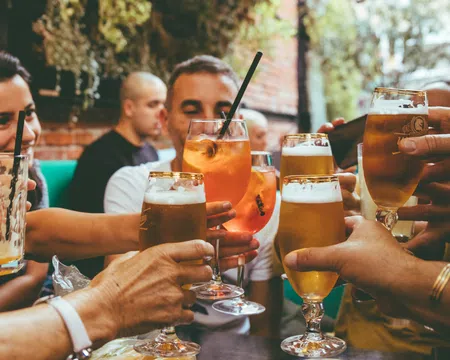 Group of friends clinking glasses with beer and cocktails at an outdoor social gathering.