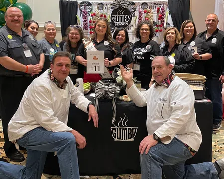 Group of people posing at Gumbo Season Fest booth with festive decorations and promotional materials.