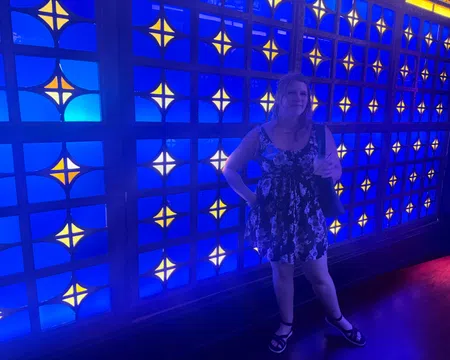 Woman in a floral dress standing in front of a vibrant blue and yellow patterned illuminated wall.