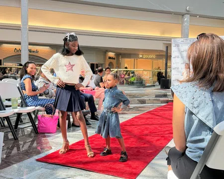 Two young models confidently posing on a red carpet runway during a fashion event in a shopping mall.