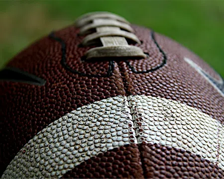 Close-up of a textured brown and white American football showing laces and pebbled surface detail.