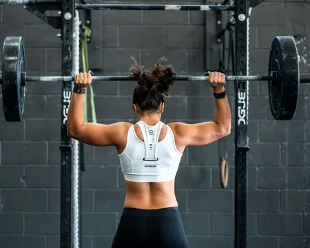 Woman lifting a heavy barbell overhead in a gym with a black brick wall background