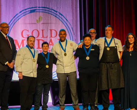 Group of chefs and officials posing with medals on stage at Gold Medal Plate culinary competition event.