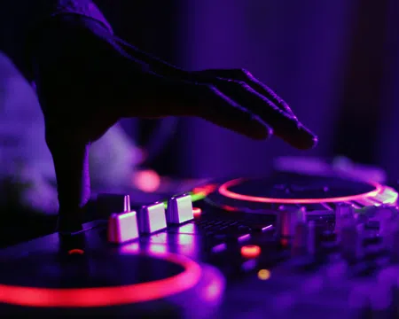 Close-up of a DJ's hand adjusting controls on a colorful illuminated mixer in a dark room.