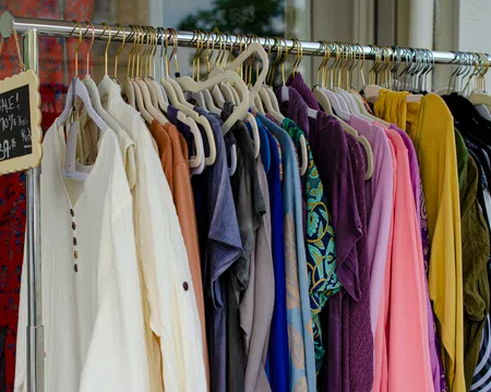 Clothing rack with diverse shirts and sweaters in various colors, with overlaid chalkboard sign showing sale details.