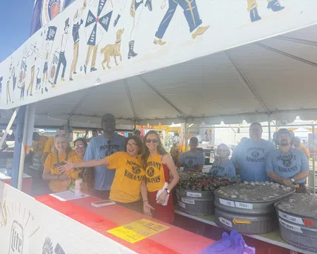 Group of Molsaint Kiwanis volunteers smiling and serving drinks under a festival tent with beer tubs.