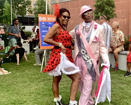 Couple dressed in vibrant retro outfits enjoying an outdoor festival on a sunny day with people relaxing nearby
