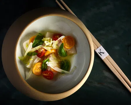 Elegant bowl of fresh vegetable salad with cherry tomatoes, greens, and chopsticks on dark surface.