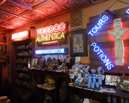 Interior of a voodoo shop with neon signs, shelves of jars, potions, dolls, and mystical items under ornate ceiling tiles.