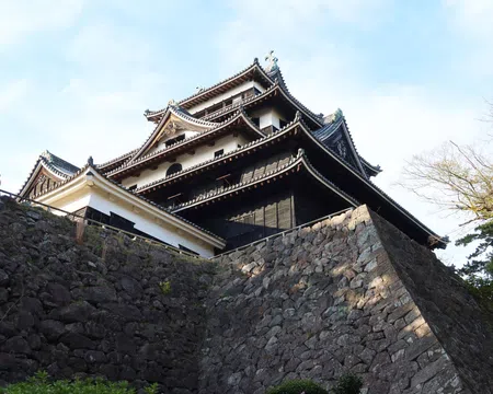 Traditional Japanese castle with multi-tiered roofs atop large stone walls under a clear sky.