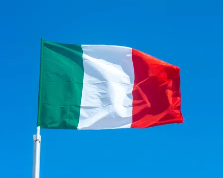 Italy national flag waving against a clear blue sky background outdoors.