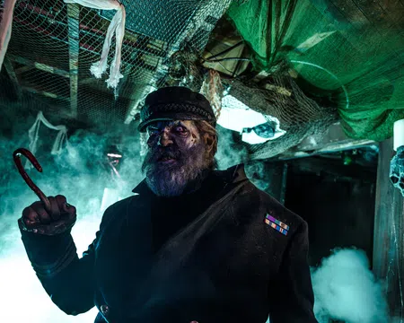 Dark haunted captain with a hook hand and eerie blue lighting in a spooky, fog-filled ship interior.