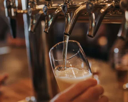 Beer being poured from a tap into a tilted glass at a bar with blurred background.
