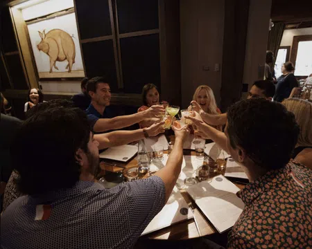 Group of friends raising glasses for a toast around a restaurant table with menus and drinks.
