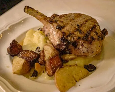 Grilled pork chop with mashed potatoes and roasted root vegetables on a white plate.