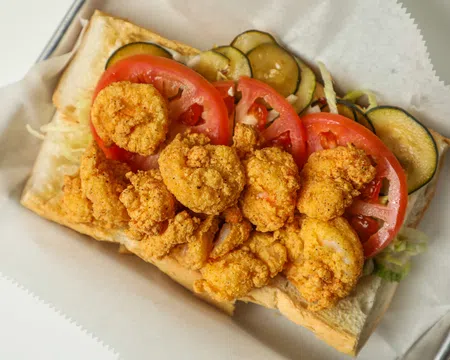 Fried shrimp po'boy sandwich with sliced tomatoes, pickles, and lettuce on a sub roll.