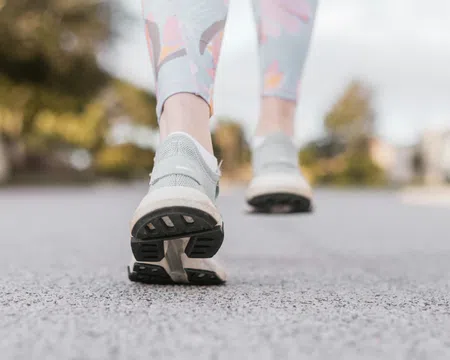 Close-up of a person walking on pavement wearing gray running shoes and floral leggings outdoors.