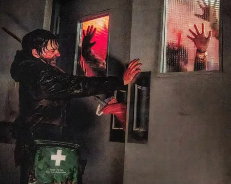 Man pushes hospital doors with bloody hands as silhouettes press against red-lit windows in a tense scene.