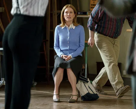 Woman in blue cardigan and black skirt sitting on a chair surrounded by blurred walking people indoors