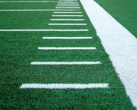 Close-up of green turf with white yard lines on an American football field.